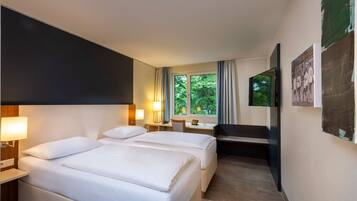 A hotel room with two beds, a desk, a chair, a TV, and a window with a view of trees.