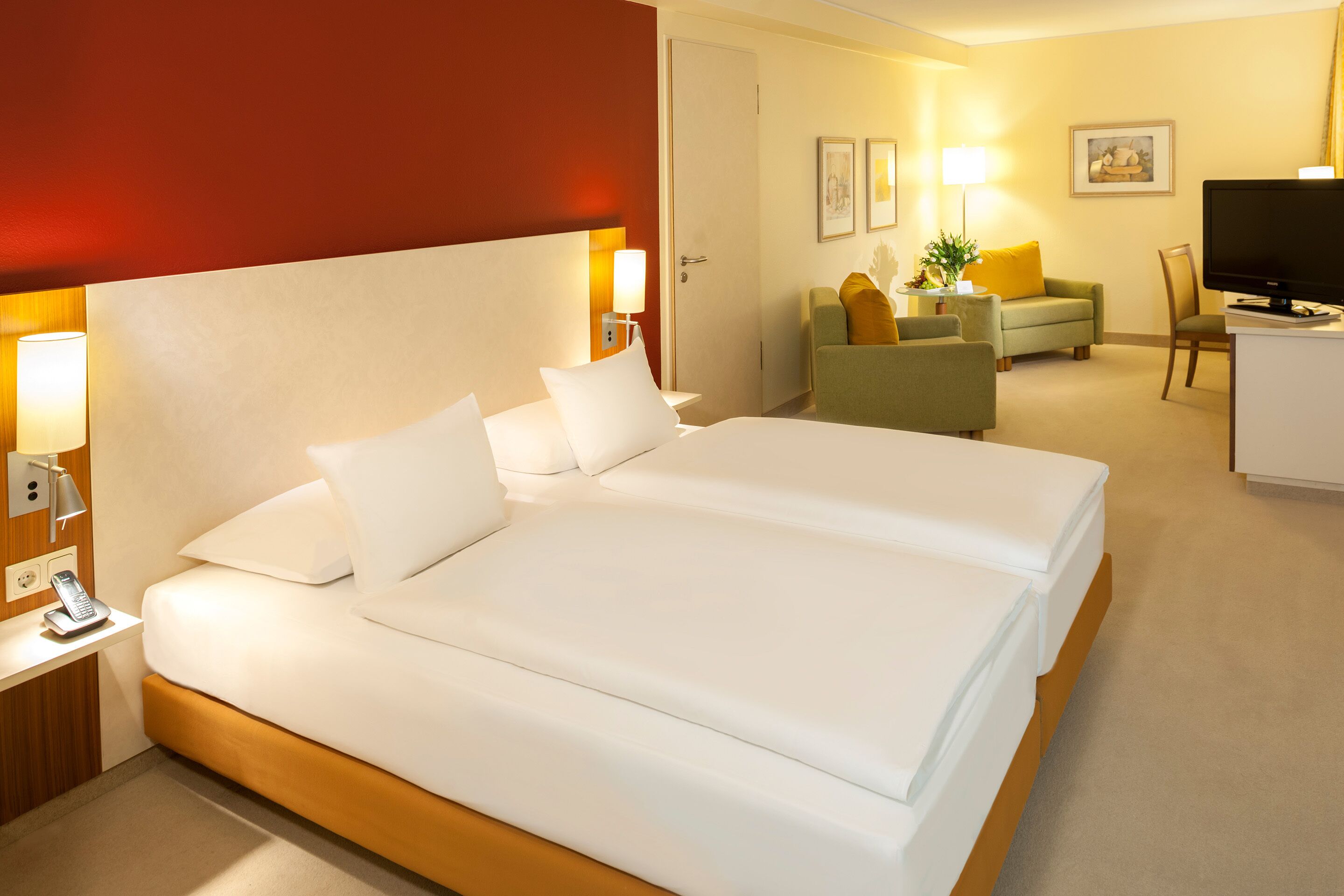 A hotel room with a large bed, a desk with a phone, a TV, and a seating area with a sofa and armchairs.