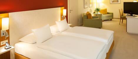 A hotel room with a large bed, a desk with a phone, a TV, and a seating area with a sofa and armchairs.