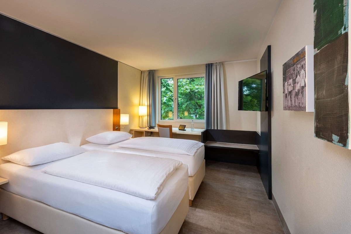 Habitación de hotel con dos camas, un escritorio, una silla, un televisor y una ventana con cortinas.
