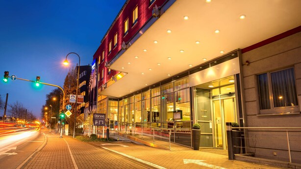 Un hotel moderno con facciata in vetro, edificio in mattoni rossi e ingresso ben illuminato.