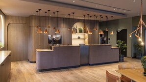 Un espace d’accueil moderne avec un comptoir de réception en bois, des luminaires suspendus et un coin salon comprenant une table et des chaises.