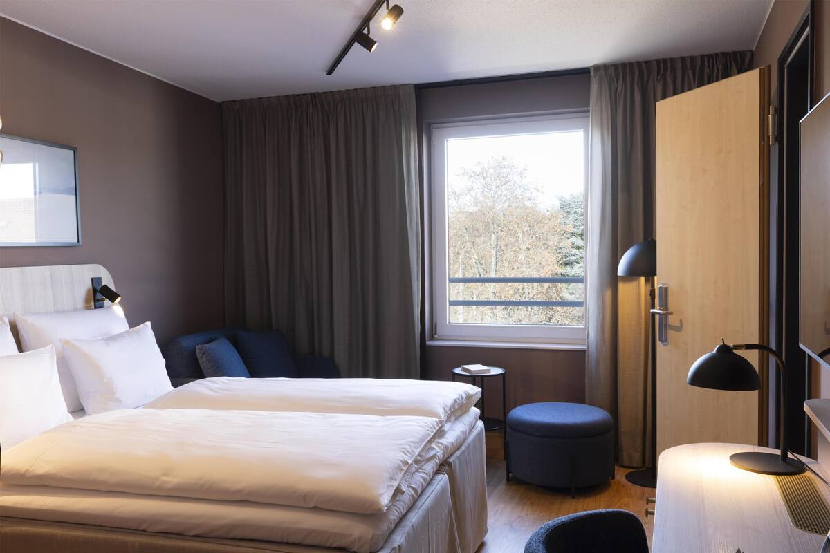 A hotel room with a large bed, a small seating area, a window with a view, and a desk with a lamp.