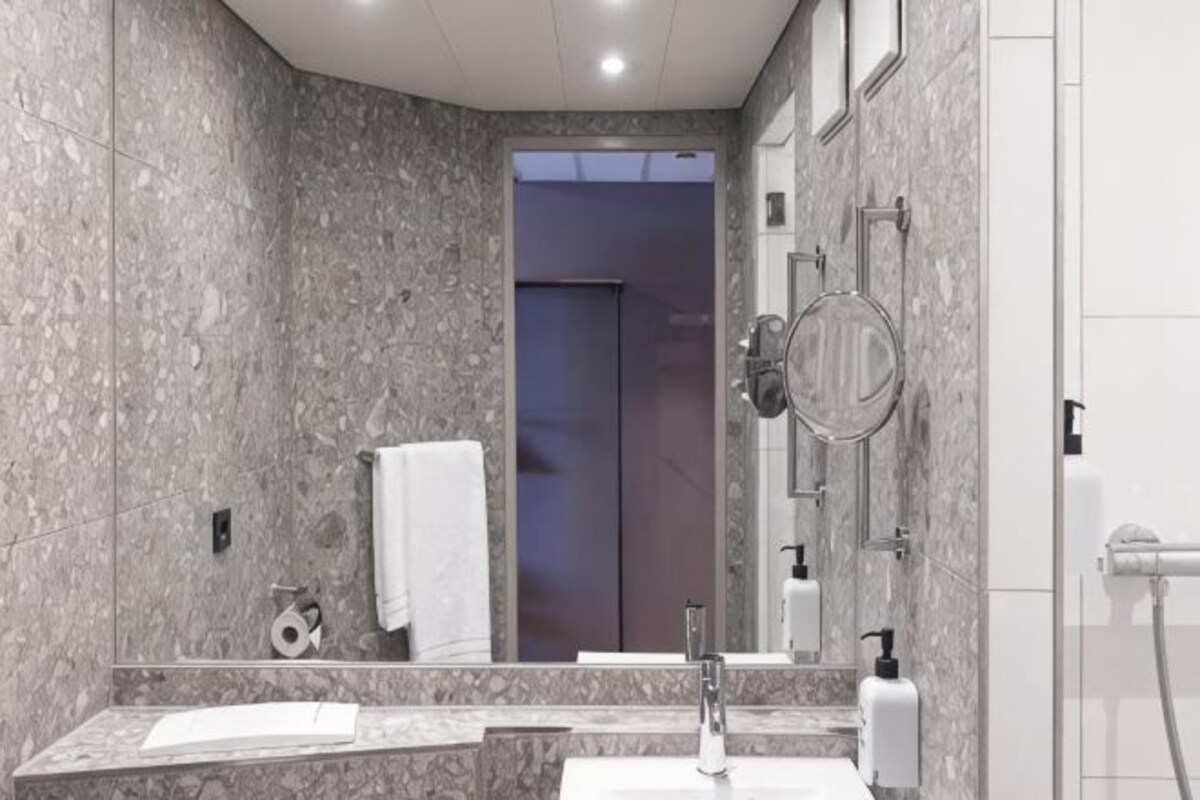 A modern bathroom with a marble wall, a sink, a mirror, and a shower area.