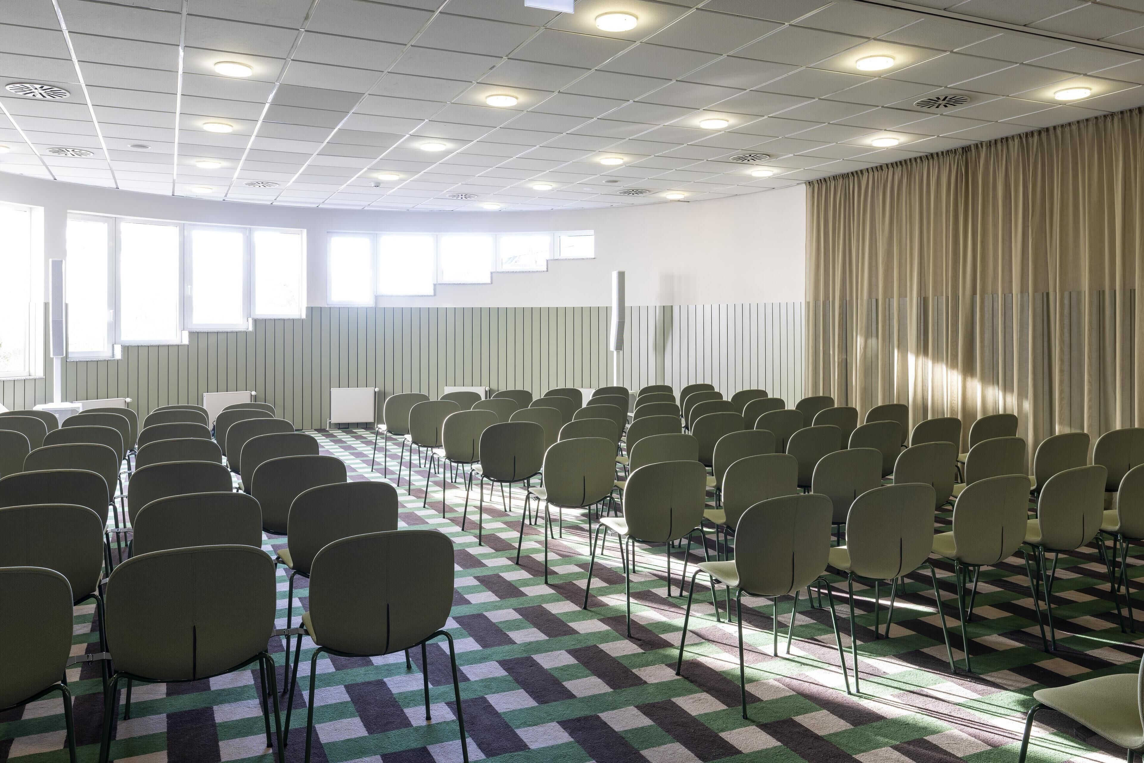A conference room with rows of chairs, a checkered floor, and a large window with curtains.