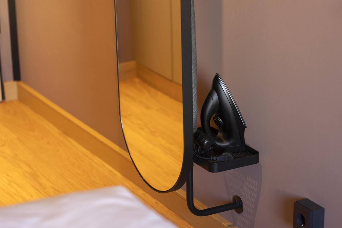A corner of a room with a wooden floor, a white bed, and a black object attached to the wall.