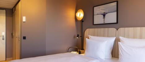 A hotel room with a bed, a nightstand, a wall-mounted lamp, and a framed picture on the wall.