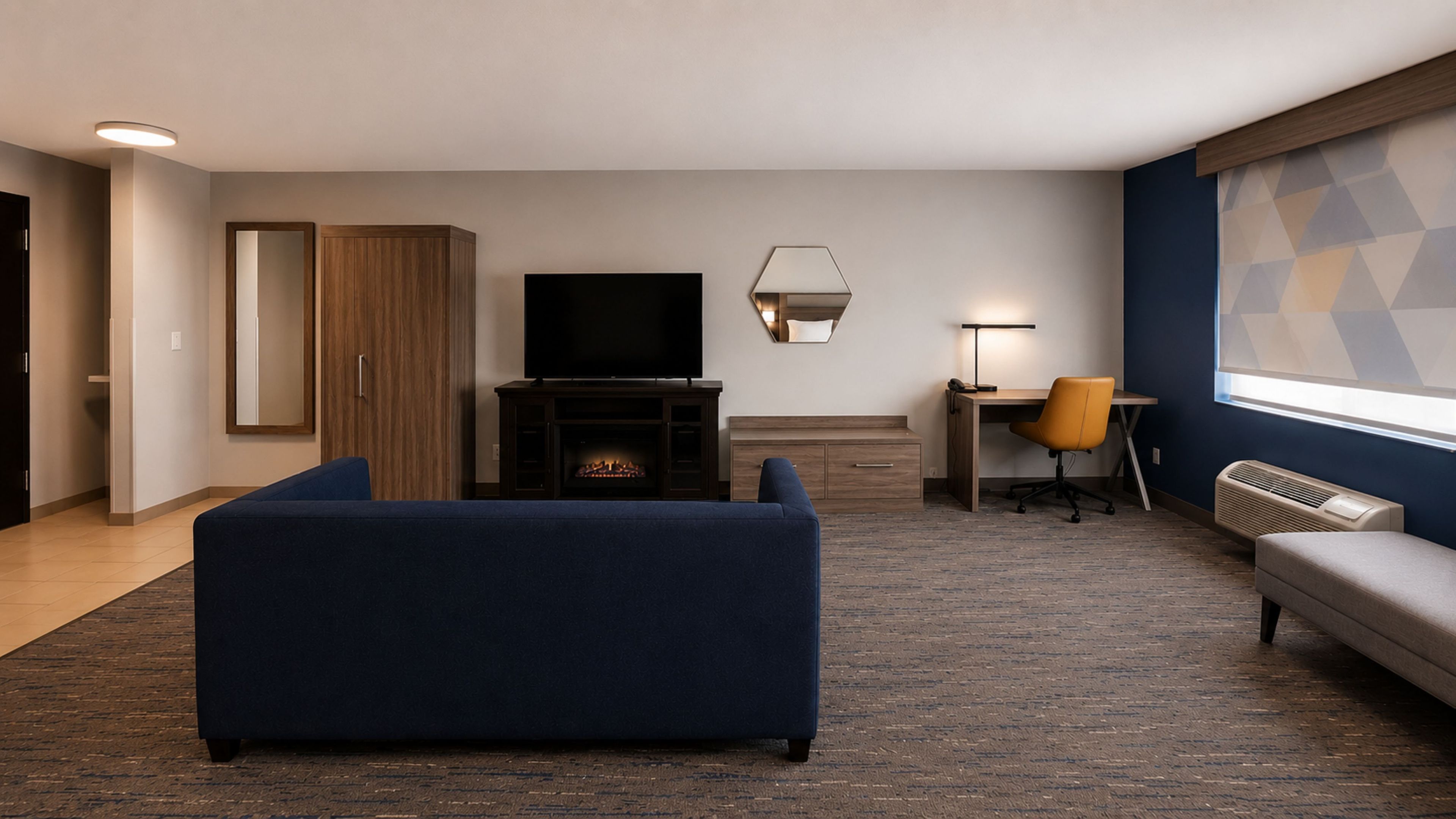 Een hotelkamer met een bank, een televisie, een bureau met een stoel, een open haard en een groot raam met een geometrisch patroon.