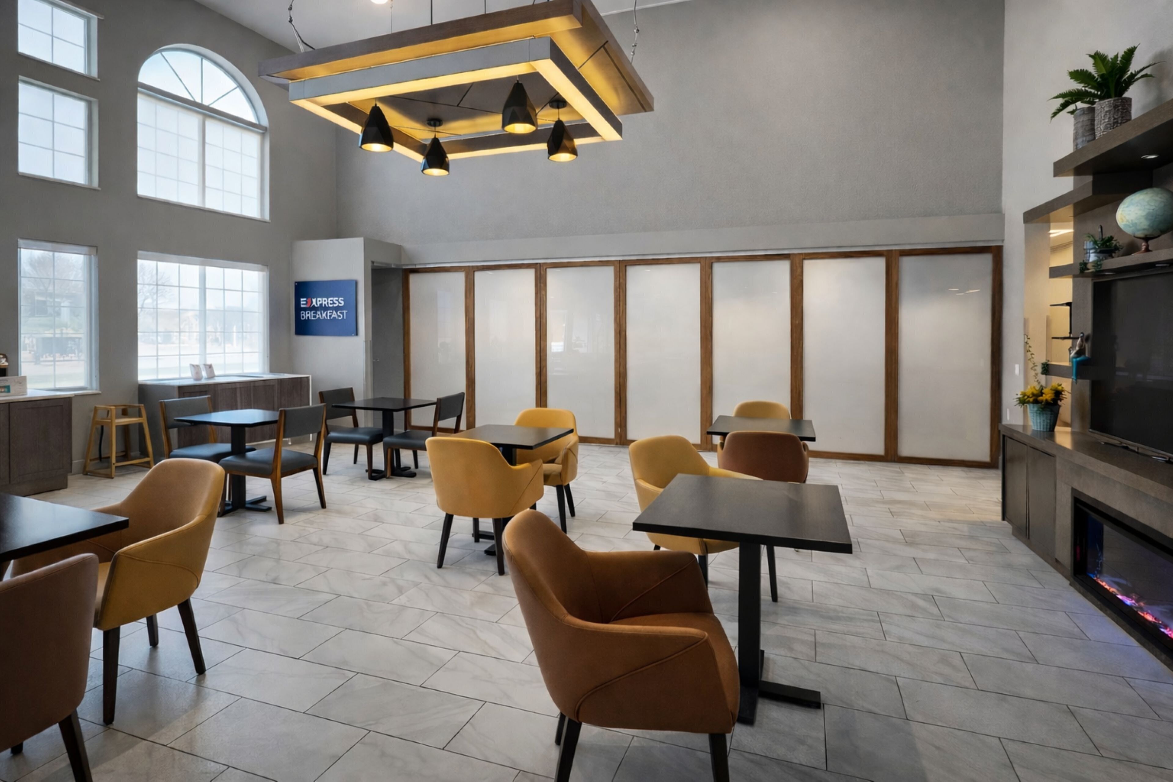 A modern dining area with tables and chairs, a fireplace, and a large window.