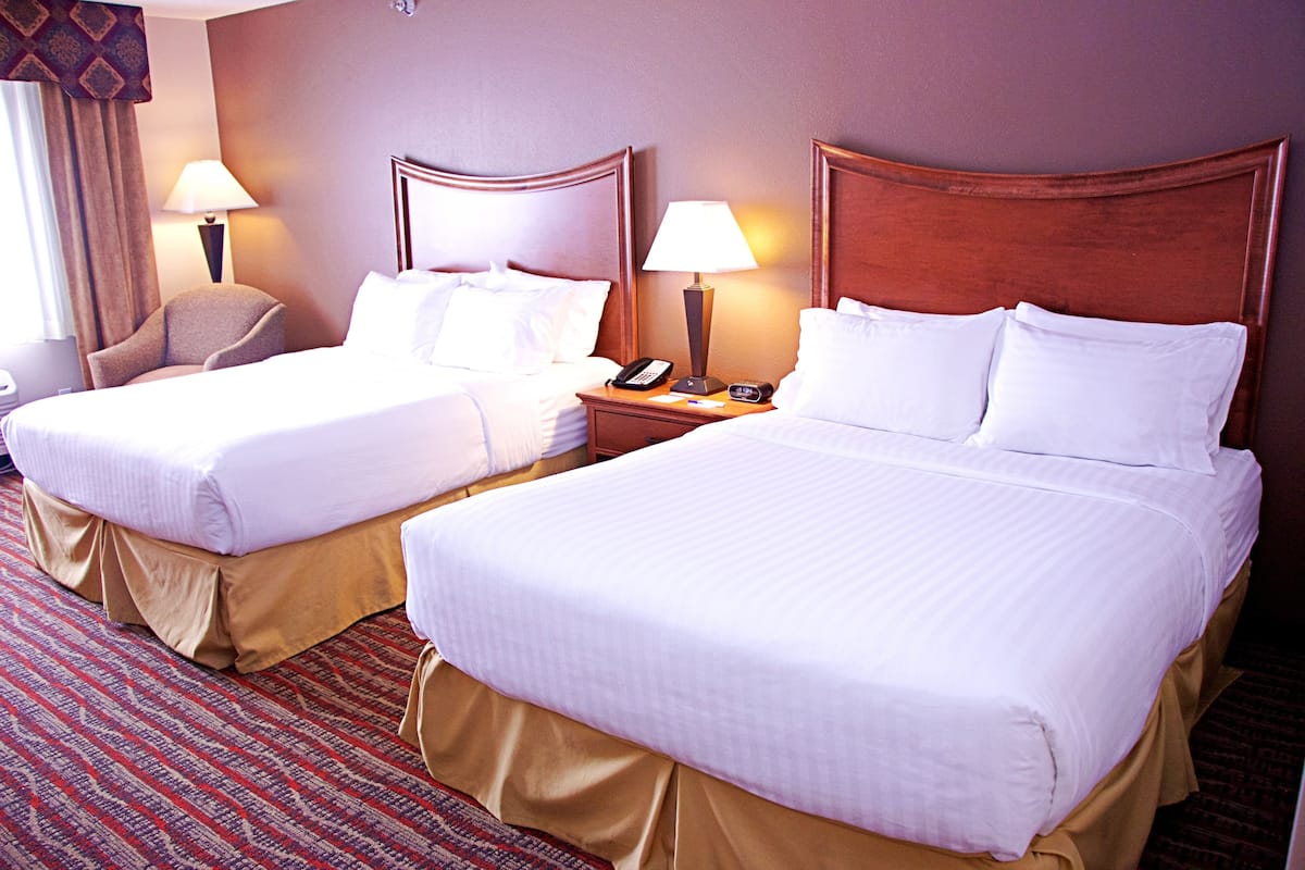 A hotel room with two beds, a chair, a nightstand with a lamp, and a telephone.