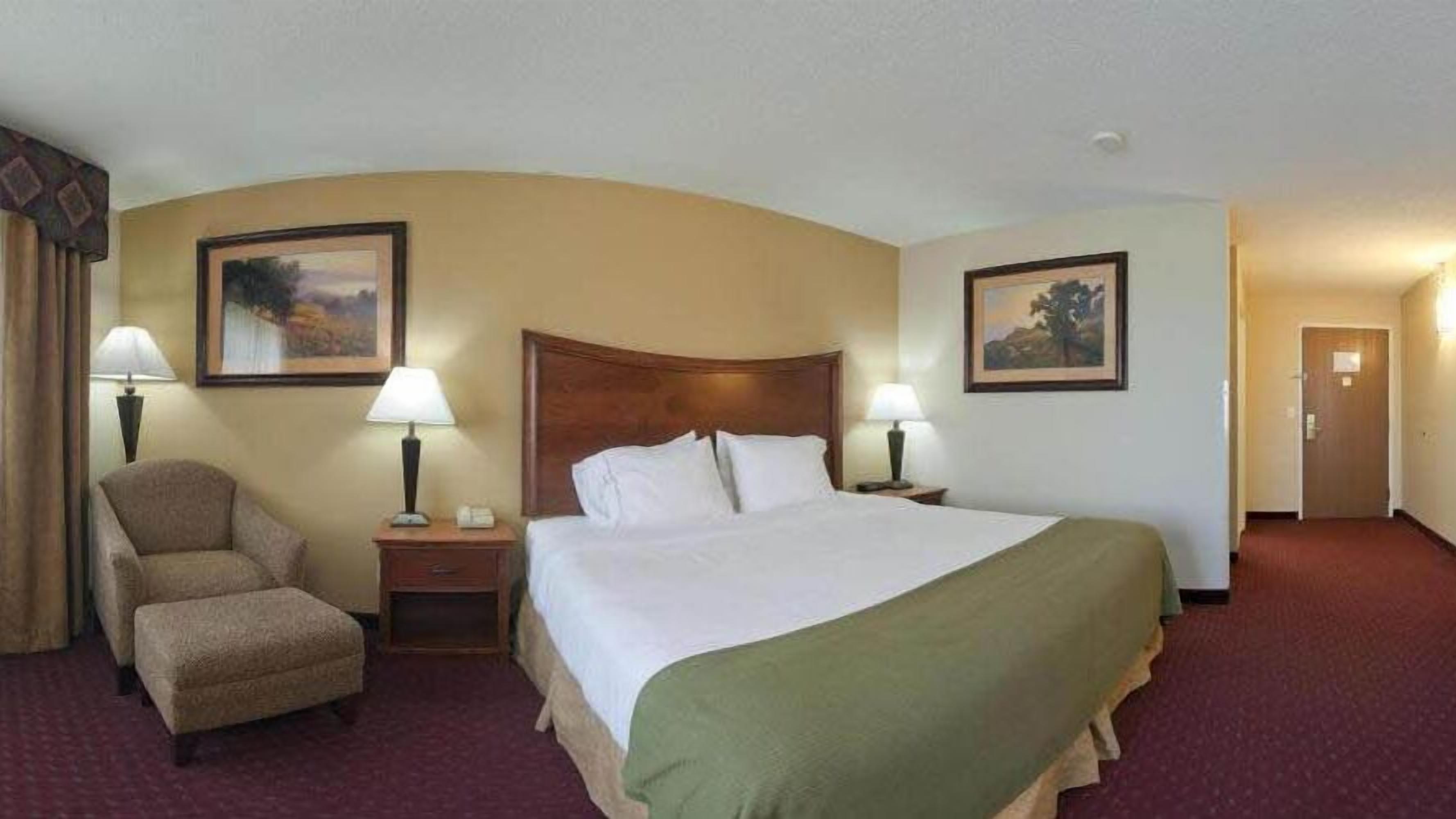 A hotel room with a large bed, two bedside tables with lamps, a chair, and two framed pictures on the walls.