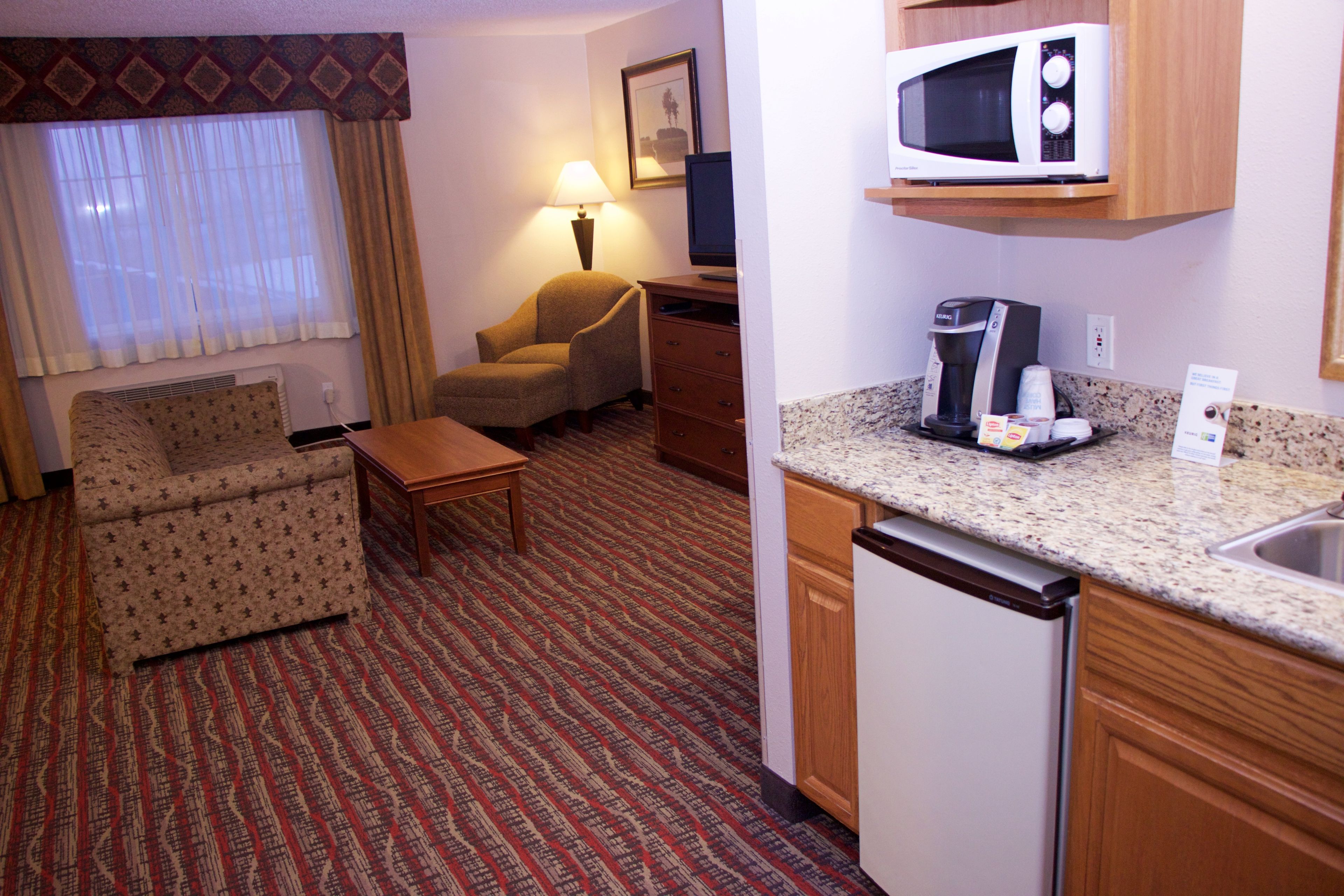 Ein Hotelzimmer mit Sofa, Sessel, kleinem Tisch und einer Küchenzeile inklusive Mikrowelle, Kaffeemaschine und Spüle.