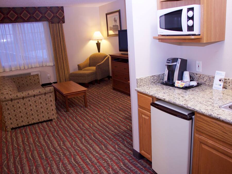 Ein Hotelzimmer mit Sofa, Sessel, kleinem Tisch und einer Küchenzeile inklusive Mikrowelle, Kaffeemaschine und Spüle.