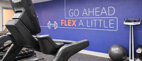 A gym with a treadmill, dumbbells, a medicine ball, and a wall with motivational text.