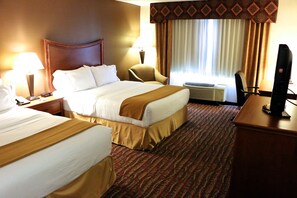 A hotel room with two beds, a desk, a TV, and a window with curtains.
