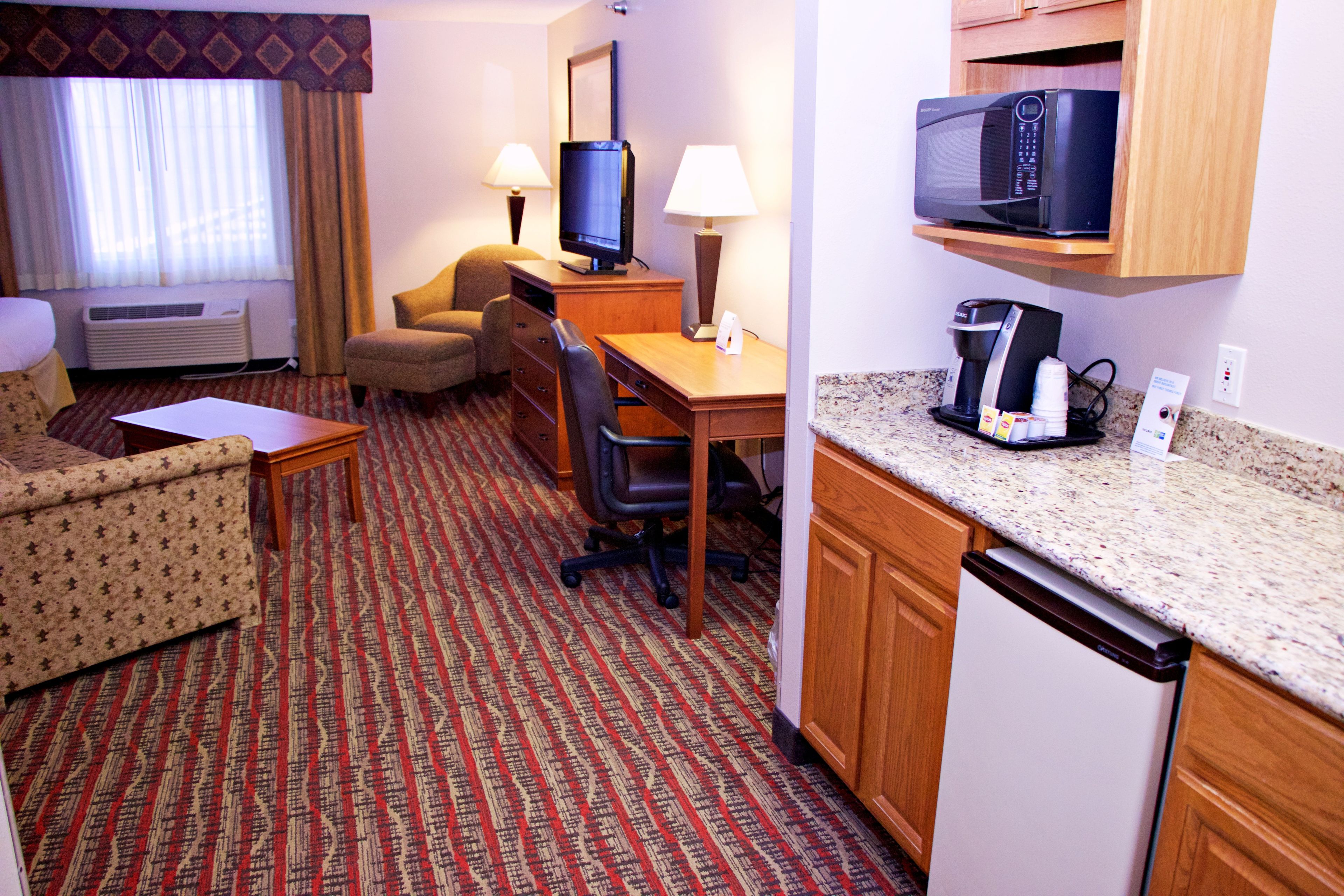 Habitación de hotel con cama, escritorio, silla, microondas, cafetera y televisor.