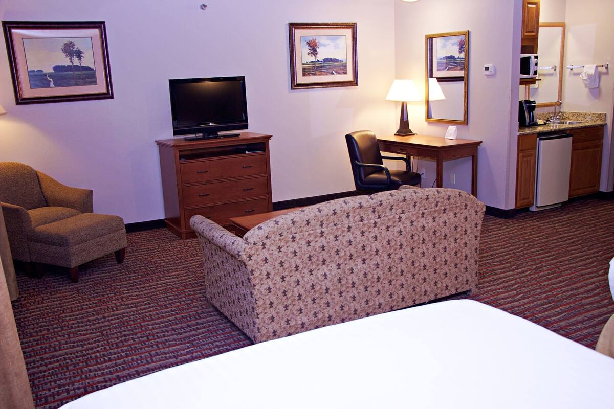 A hotel room with a bed, a desk, a chair, a television, a small kitchenette, and a bathroom.