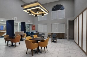 A spacious indoor area with multiple tables and chairs, a high ceiling with pendant lighting, large windows, and a view of the sky. - Holiday Inn Express & Suites Fort Pierre by IHG (Fort Pierre)