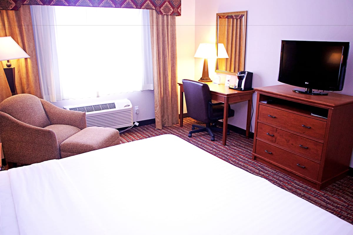 A hotel room with a bed, a desk with a chair, a television, a lamp, and a dresser.