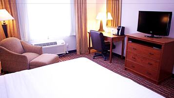 A hotel room with a bed, a desk with a chair, a television, a lamp, and a dresser.