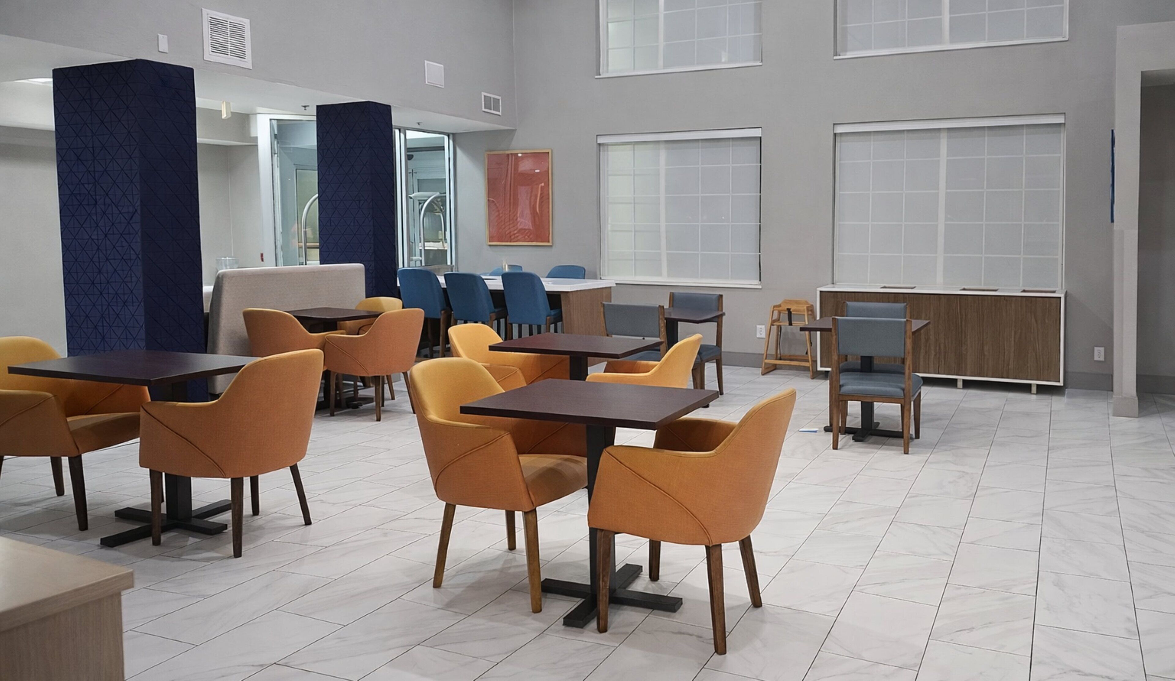 Un espace repas moderne avec des tables et des chaises, de grandes fenêtres et un mur d’accent bleu.