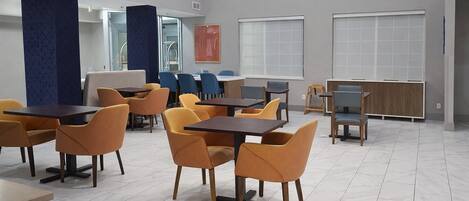 Un espace repas moderne avec des tables et des chaises, de grandes fenêtres et un mur d’accent bleu.