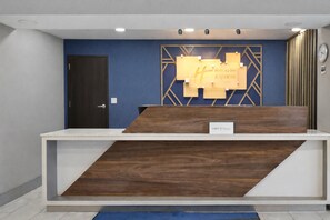 A reception desk with a wooden finish, a blue wall, and a clock on the right. - Holiday Inn Express & Suites Fort Pierre by IHG (Fort Pierre)