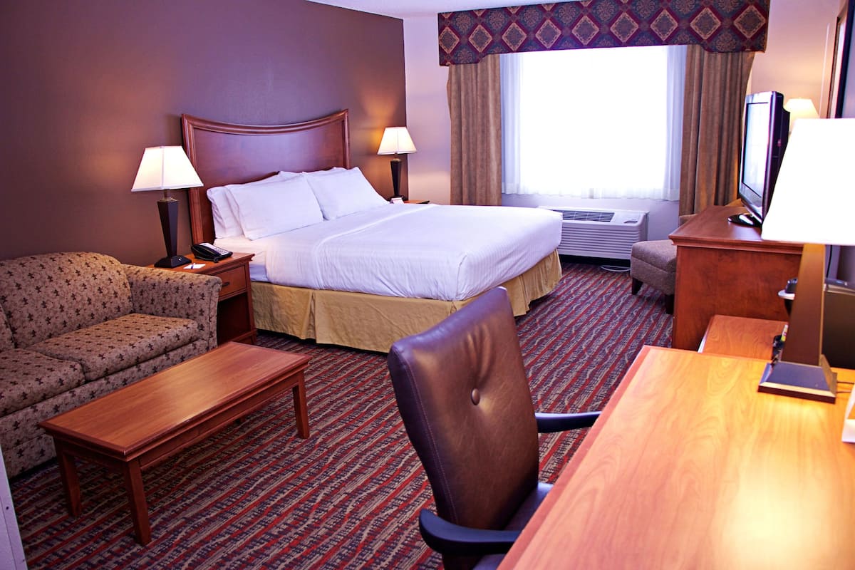 A hotel room with a bed, a sofa, a desk, a chair, and a television.