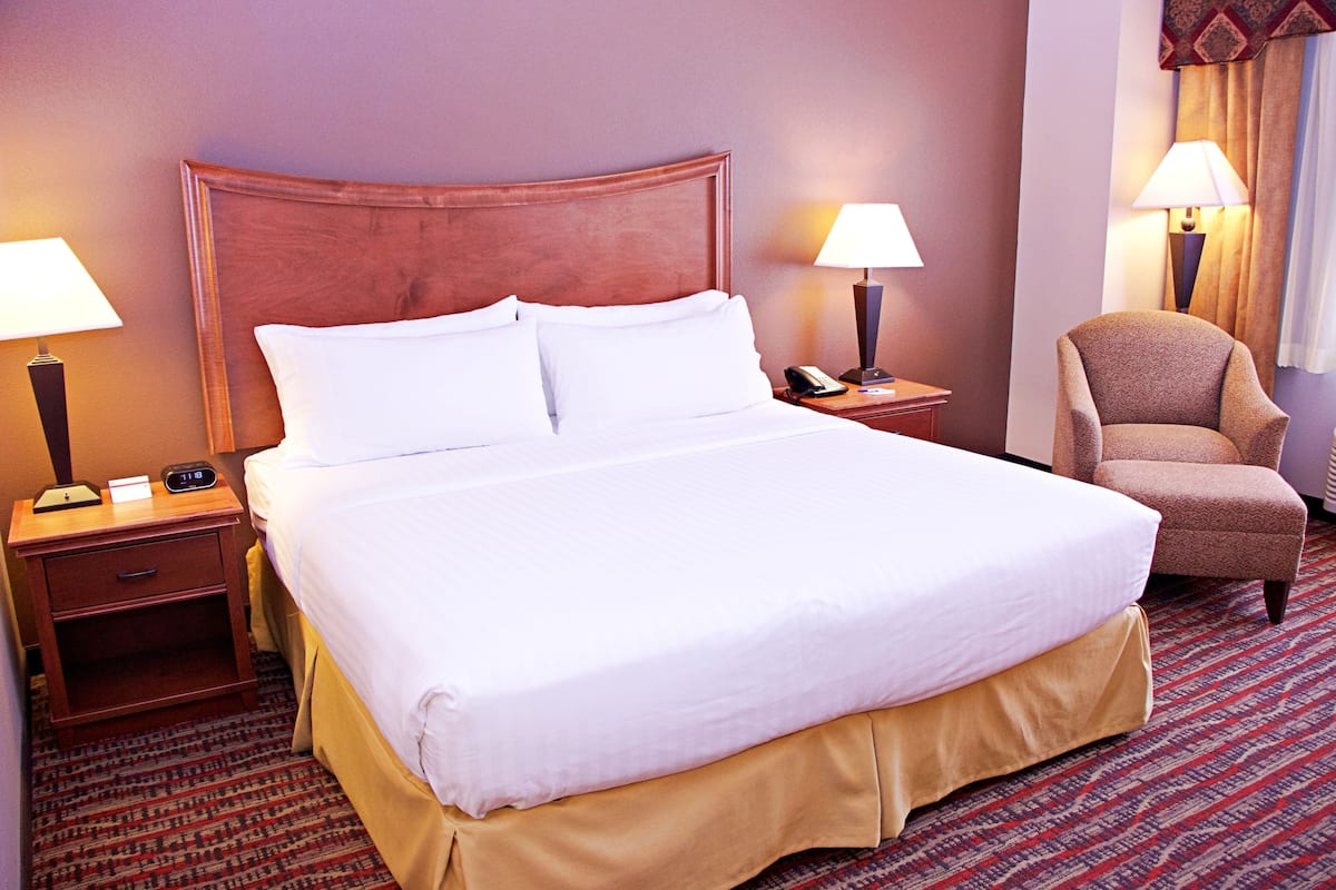 A hotel room with a large bed, two bedside tables with lamps, a chair, and a patterned carpet.