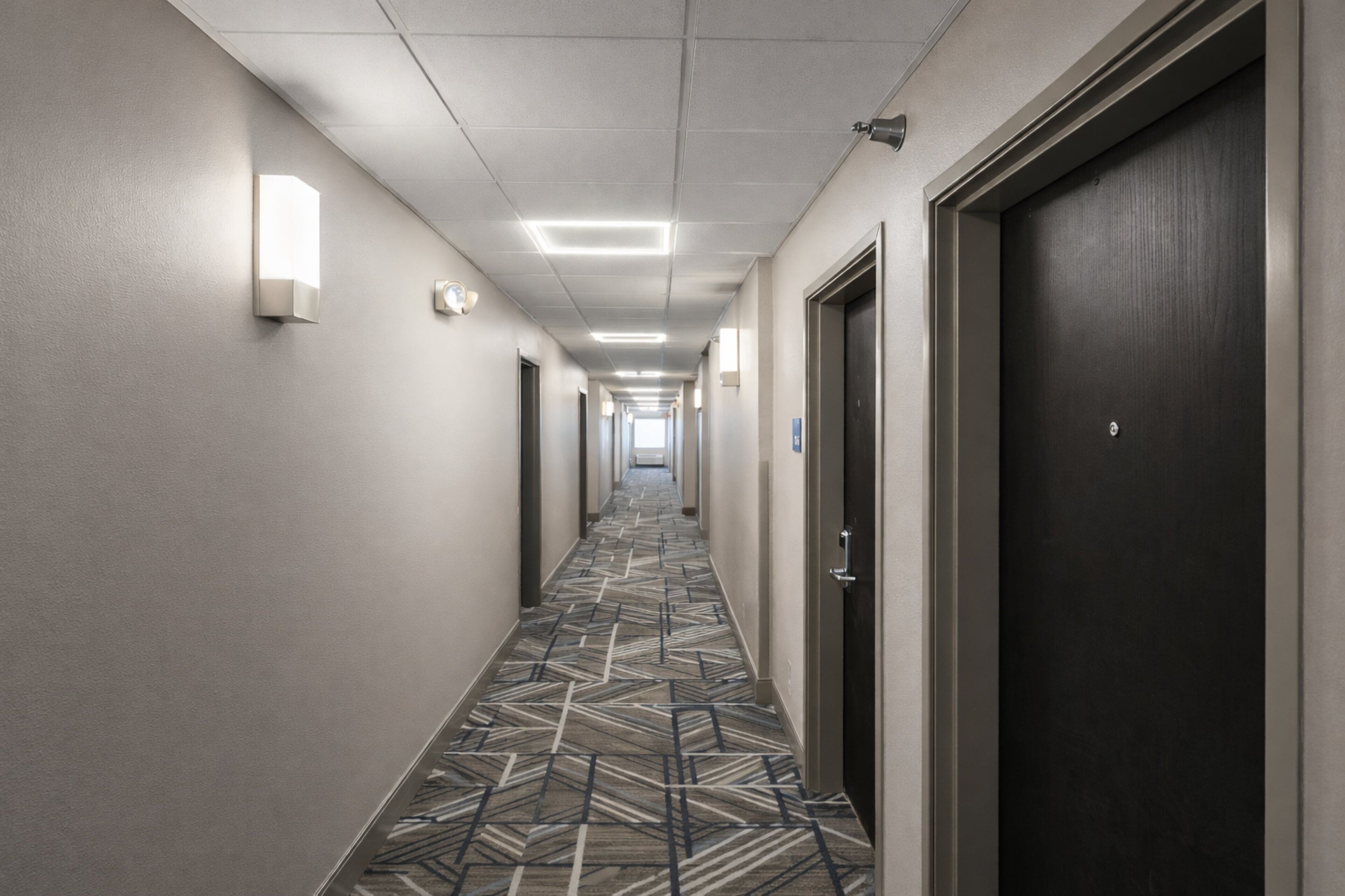 A hotel hallway with patterned carpet, doors, and wall-mounted lights.