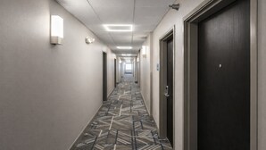 A hotel hallway with patterned carpet, doors, and wall-mounted lights.
