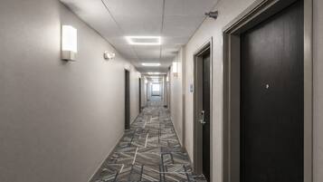 A hotel hallway with patterned carpet, doors, and wall-mounted lights.