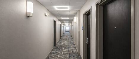 A hotel hallway with patterned carpet, doors, and wall-mounted lights.