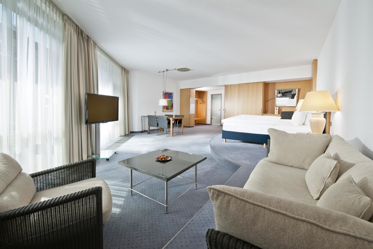 Ein Hotelzimmer mit einem Bett, einem Fernseher, einem Schreibtisch und einer Sitzecke mit Tisch und Stühlen.