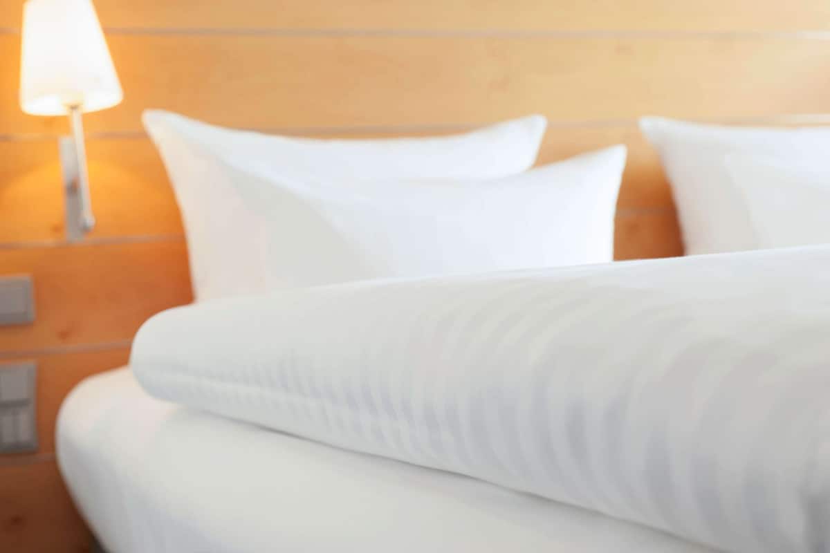 Habitación de hotel con una cama bien tendida, una lámpara de pared y un cabecero de madera.