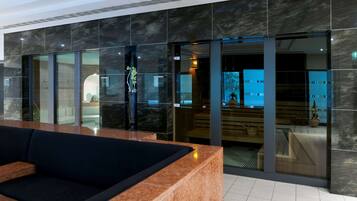 A modern lobby with a reception desk, seating area, and a glass door leading to a spa area.