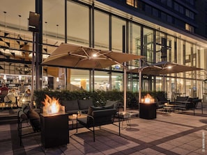 Een terras met vuurkorven en parasols, een bar op de achtergrond en een moderne gevel.