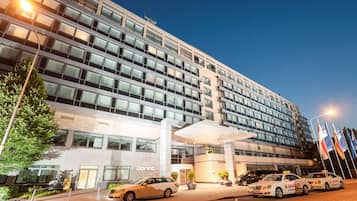 Ein modernes Hotel mit einer großen Glasfassade, mehreren Stockwerken und einem markanten Eingangsbereich mit Vordach.