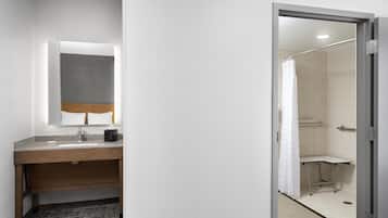 A bathroom with a wooden vanity, a mirror, a sink, and a shower area.