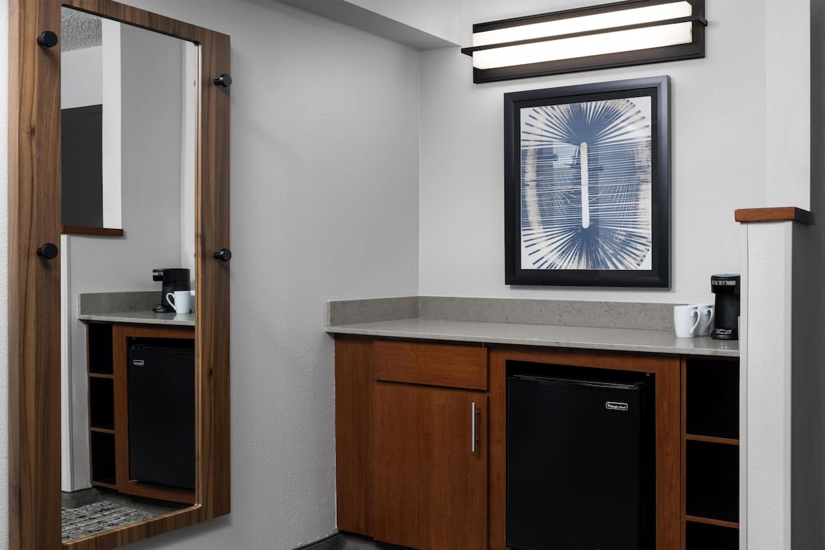 Un baño pequeño con tocador de madera, un refrigerador negro y una obra de arte abstracta enmarcada en la pared.