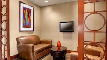 A room with a brown leather sofa, a small round table with a red vase, a flat-screen TV mounted on the wall, and a wooden partition with circular cutouts.