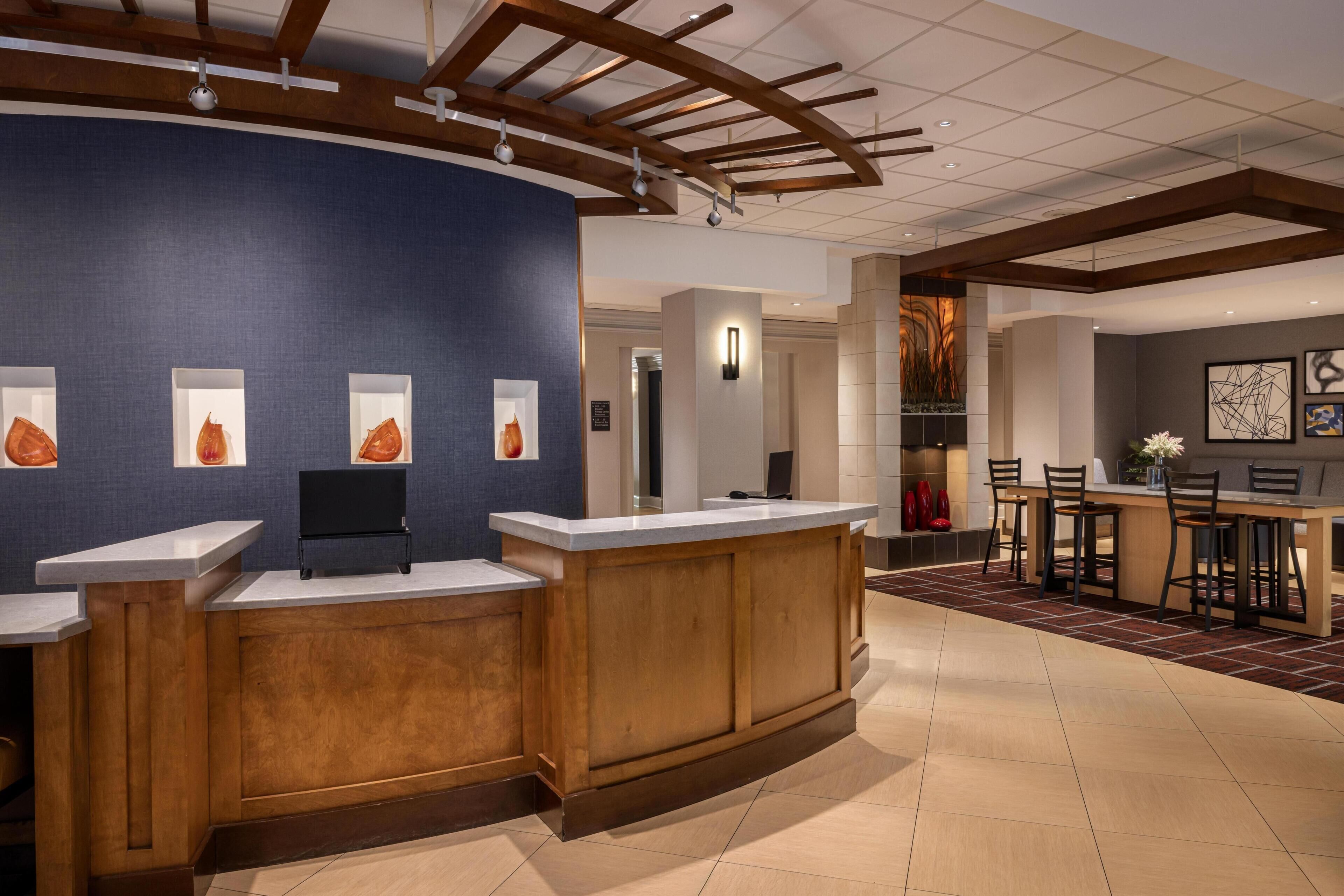 A reception area with a curved wooden desk, a blue wall with framed pictures, and a modern kitchen with bar seating.