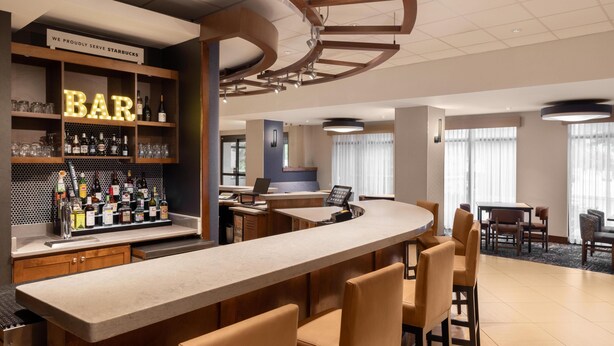 A bar area with a counter, bar stools, shelves with bottles, and a sign indicating it serves Starbucks. - Hyatt Place Charlotte Airport/Lake Pointe (Charlotte)