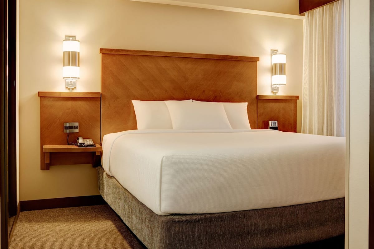 A hotel room with a large bed, wooden headboard, bedside lamps, a phone, and a small table.