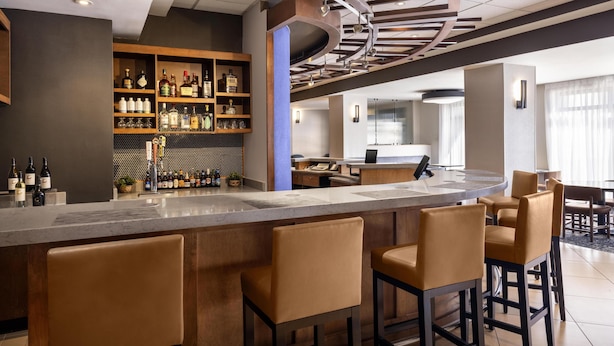 A bar area with a curved ceiling, bar stools, and shelves stocked with bottles.