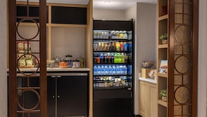 A compact kitchenette with a refrigerator stocked with beverages, a small sink, and a cabinet with kitchen essentials.