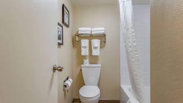 A bathroom with a toilet, a towel rack with towels, a framed picture, and a shower curtain.