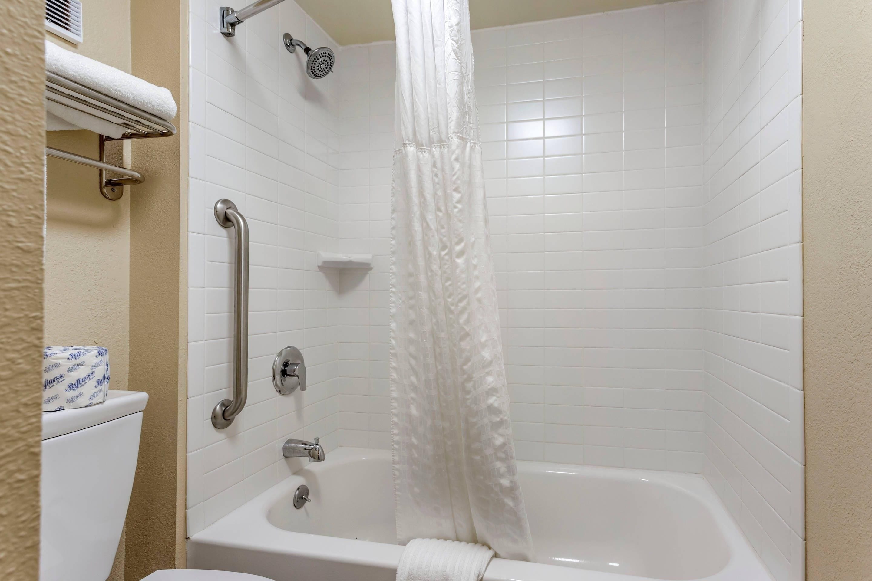 A bathroom with a white bathtub, a shower with a handheld showerhead, a grab bar, and a towel rack.