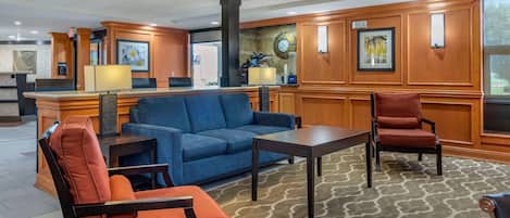 A lobby with a reception desk, blue sofa, armchairs, and a patterned carpet.