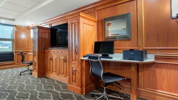Quarto de hotel com armários de madeira, uma mesa com computador, uma cadeira e uma janela grande.
